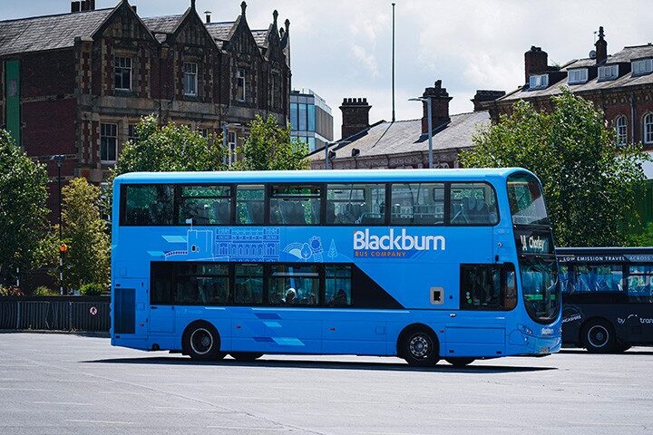 A blue Blackburn Bus Company double-decker bus parked in a bus station area with buildings and trees behind it.
