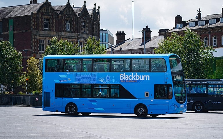 A blue Blackburn Bus Company double-decker bus parked in a bus station area with buildings and trees behind it.