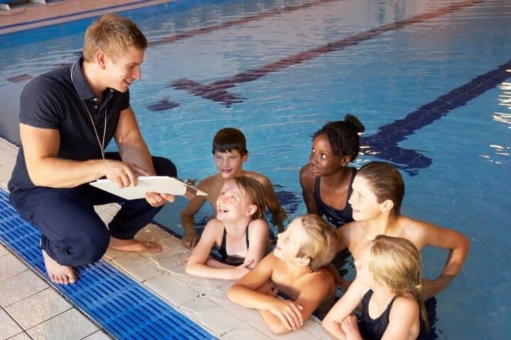 Swimming coach talking to children in swimming pool whilst they listen