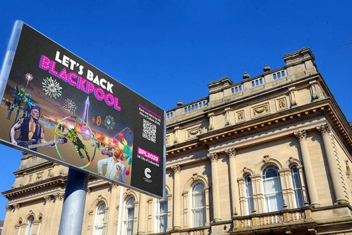 A large digital billboard promoting “LET’S BACK BLACKPOOL” outside a historic stone building.