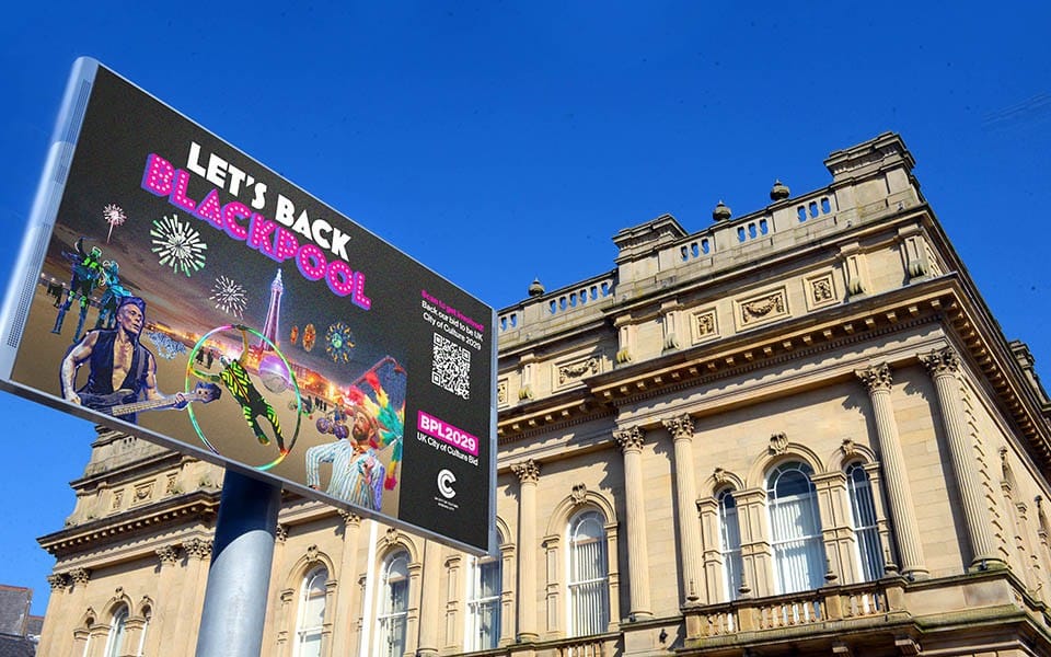 A large digital billboard promoting “LET’S BACK BLACKPOOL” outside a historic stone building.
